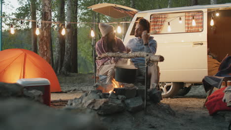 couple talking at campsite while cooking food over fire