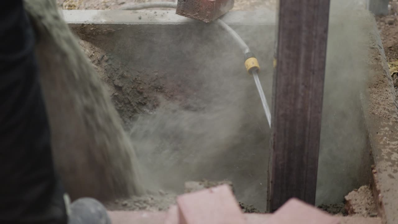 hosing the concrete mix at base of a timber post that has been installed in the ground
