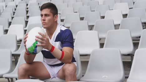 jugador de rugby hombre sentado con una pelota de rugby en el estadio 4k