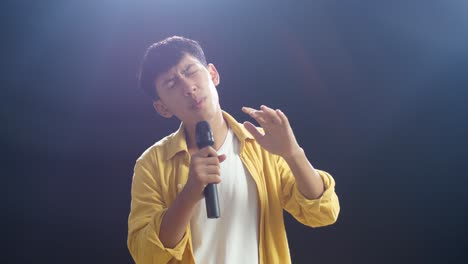 young asian boy holding a microphone and singing on the black background