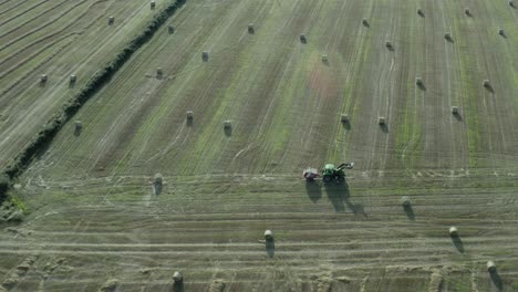 aerial: tractor with baler drives over green hay field of round bales