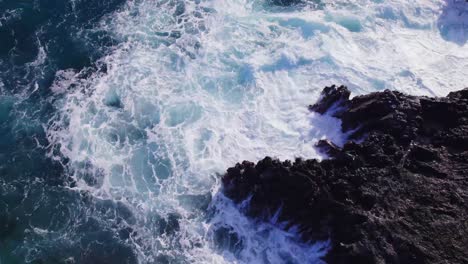 drone-footage-beginning-with-white-capped-waves-crashing-violently-against-a-rocky-cliff-and-ascending-to-reveal-the-vast-blue-Pacific-Ocean-and-its-overall-calmness-at-island-of-Oahu-Hawaii