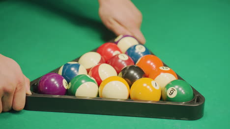 cerca de las manos asegurando el estante triangular con bolas de billar de colores bien dispuestas en la mesa de billar verde. colores vibrantes contrastan con el fondo oscuro, capturando un enfoque intenso antes de comenzar el billar