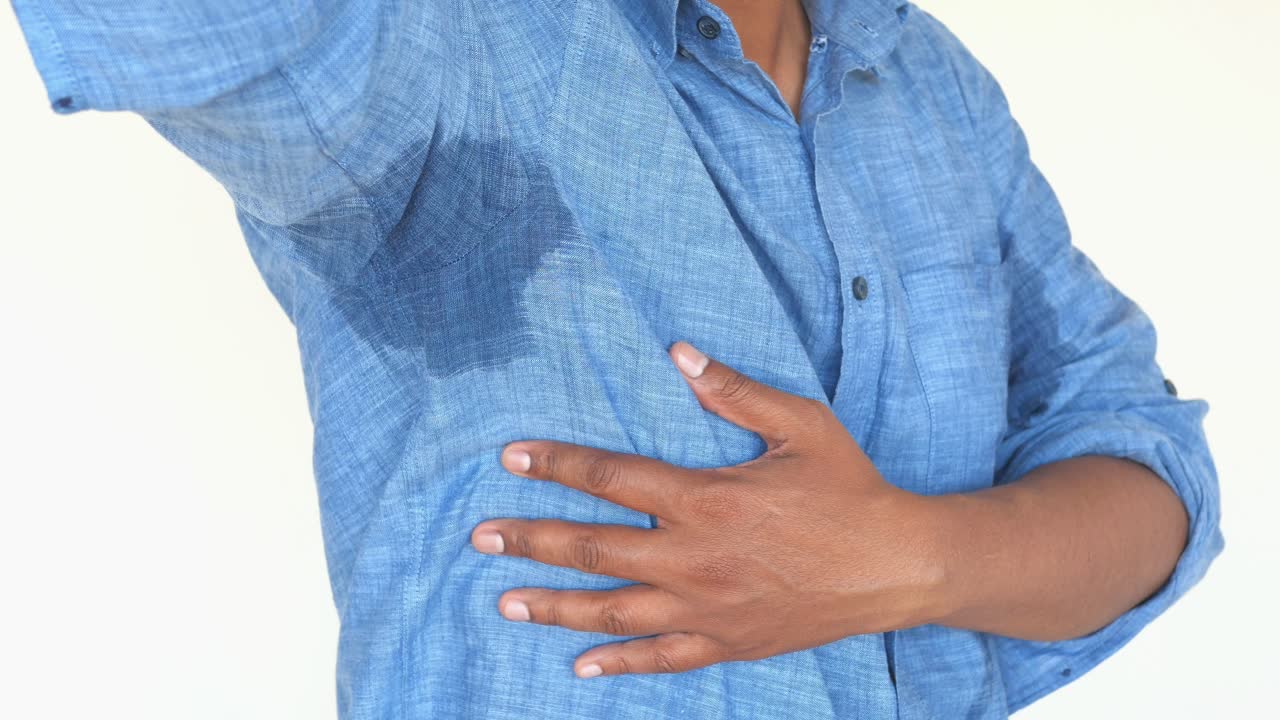 área de las axilas sudorosa en una camisa azul claro
