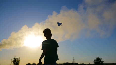 kid playing with plane. smiling boy playing with flying paper airplane toy outdoors at sunset