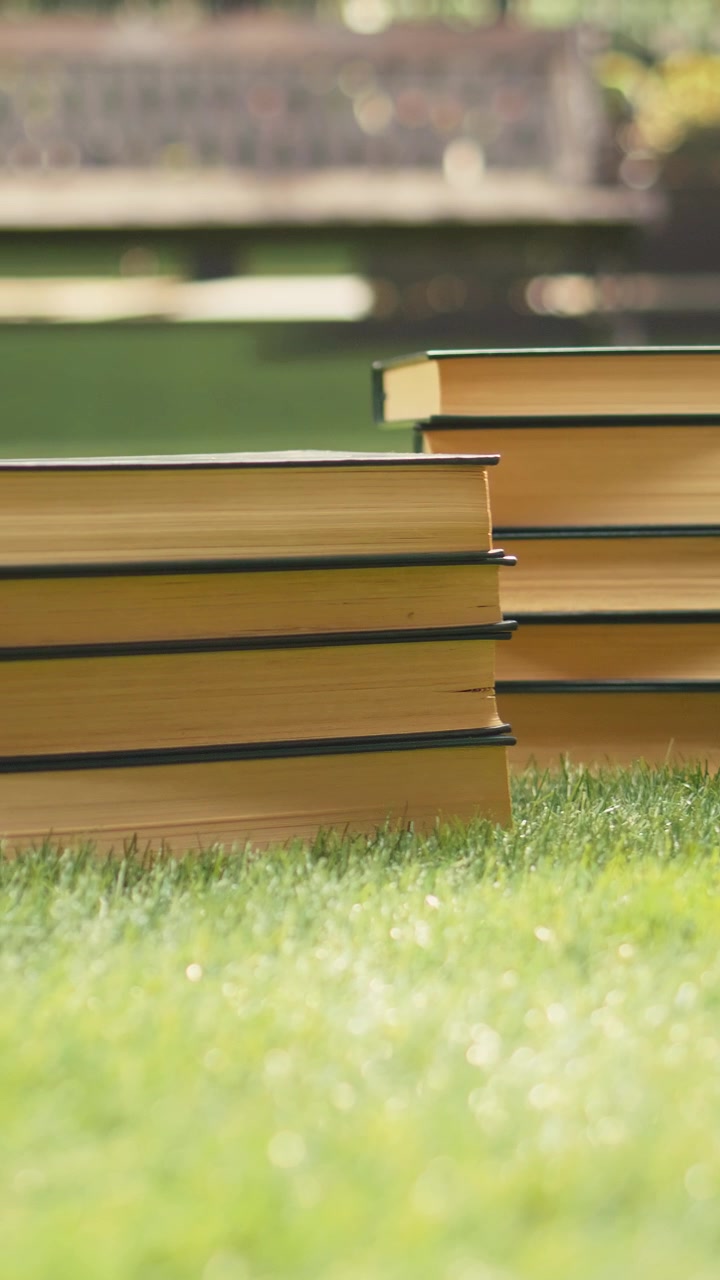 Vertical Video Close up of stacked books placed on sunny campus lawn with modern study area