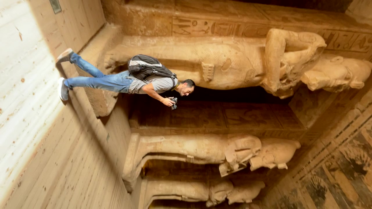 Turista s fotoaparátem prozkoumávající chrám Abú Simbel Ramesse II. v Egyptě. Cestovatel uvnitř chrámu Abú Simbel. Turista na výletě sledující sochy faraona Ramesse II. Touha cestovat, vertikální.