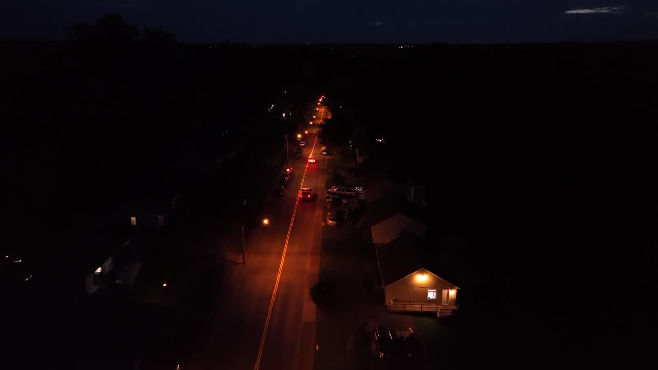 Aerial tilt up of car on lighting street at night. Suburb district of american town in quiet housing area. Wide shot.