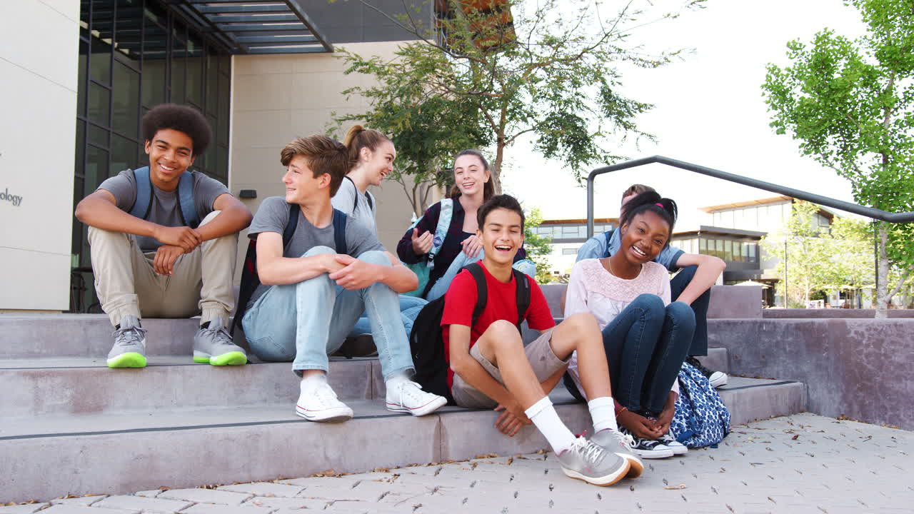 retrato de un grupo de estudiantes de secundaria sentados fuera de los edificios de la universidad