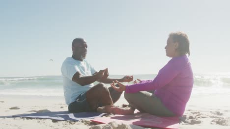 senior african american couple practicing yoga and meditating on sunny beach