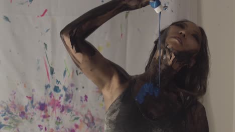 a stunning asian female model is pouring blue body paint on herself