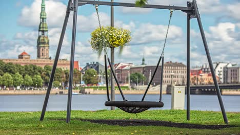 timelapse shot of an empty swing beside a river during the morning time with the view old buildings in the background on a cloudy day