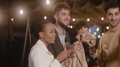 portrait of group of four happy multiethnic friends taking a selfie video and toasting with champagne glasses at new year's eve party 4