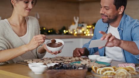 multi ethnicity couple decorating sweet cookies at home during the christmas.