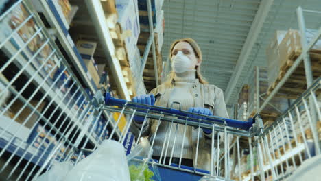 a woman wearing a mask and protective gloves walks with a shopping trolley at the supermarket