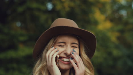 close-up view of caucasian young blonde woman wearing a hat and talking on the phone and laughing in the park in autumn