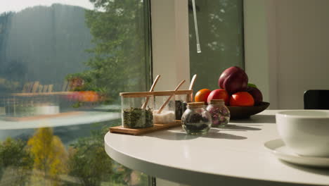 tabletop hosts porcelain cup jars and fruits. array of aromatic spices and dried herbs and assortment of nourishing fruits grace kitchen setting