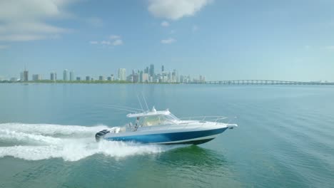 the yacht, moving through the blue-green sea, is accompanied by white waves and a clear blue sky above the city of miami