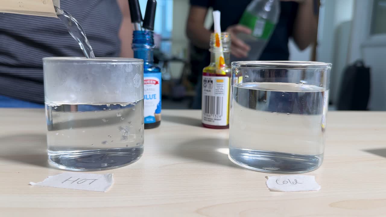 Two glasses labeled hot and cold filled with water, bright indoor lighting, stable camera angle