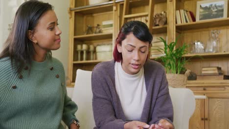 Sad-biracial-sisters-sitting-on-sofa-and-talking-and-comforting,-in-slow-motion