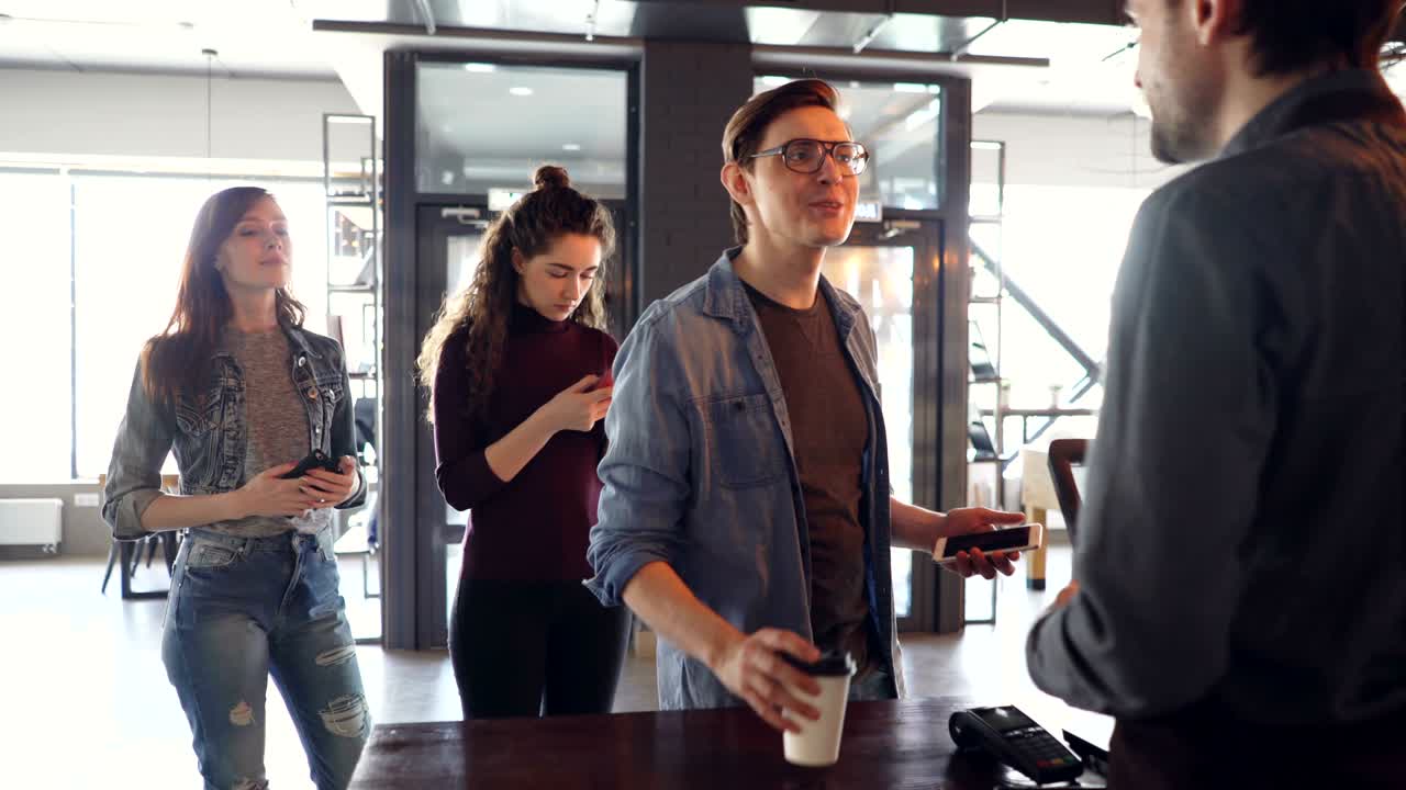 Jovens fazem fila comprando café para viagem e pagando com celular em um café pela manhã. Conceito de negócio bem-sucedido e banca moderna.