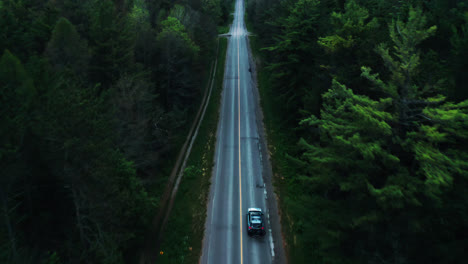 aerial flyover of car driving through empty atmospheric forest highway road surrounded by trees