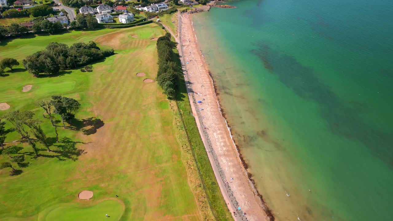 High reversing aerial video of Helen's Bay beach in County Down, Northern Ireland, UK on a bright summer day. Filmed in 4K, 60FPS and with Rec709 color