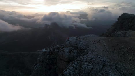 hiker on dramatic cliff's edge on dolomites mountaintop, cinematic aerial orbit