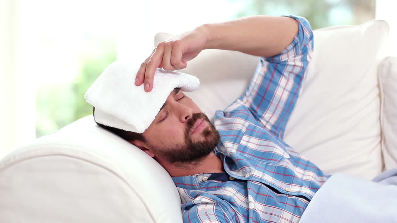 Sick man taking his temperature on the couch