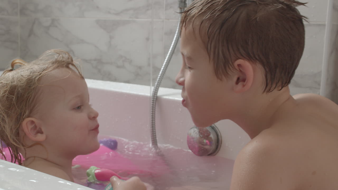 A baby girl and her brother playing in the bath