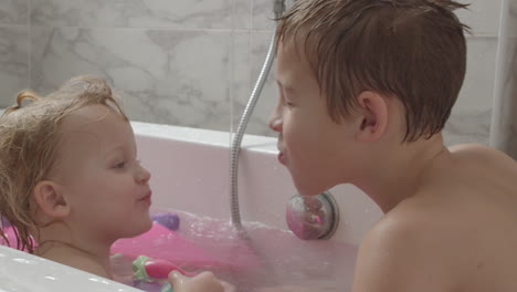 a baby girl and her brother playing in the bath