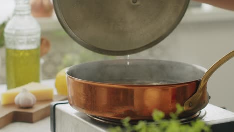 faceless person opening pan lid while cooking in kitchen