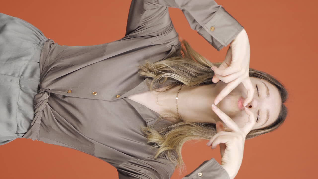 video vertical de una mujer joven haciendo una señal de corazón a la cámara.