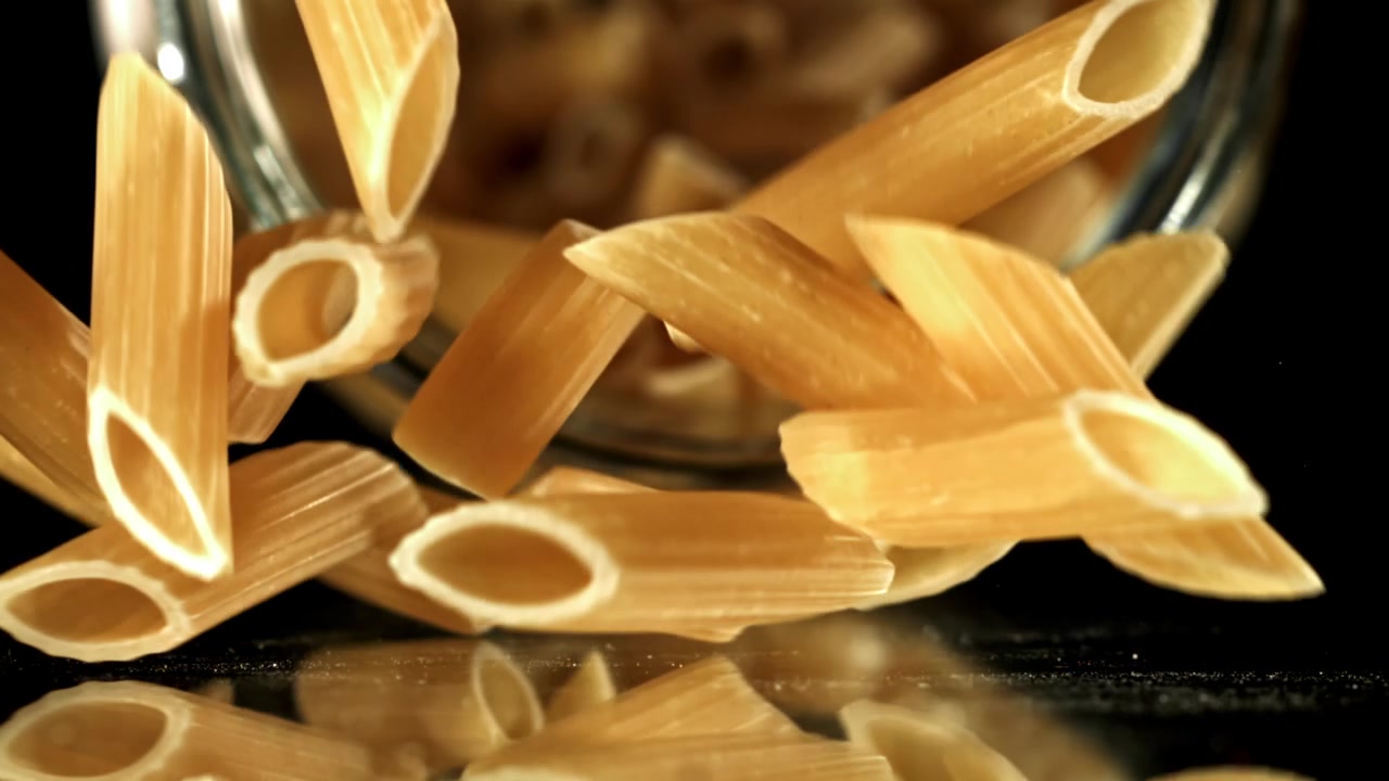 Rallentatore di pasta penne secca che cade su una superficie riflettente nera