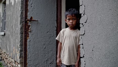 young boy leaning against weathered doorway, reflecting deep curiosity and subtle apprehension within challenging living environment, embodying resilience of childhood amid socioeconomic hardship