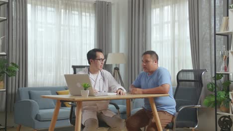 asian male doctor with a fat male patient in clinic, sitting at desk, discussing about the results of medical check up on a laptop, giving bad news, encouraging a patient