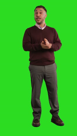 man in a brown sweater and grey pants standing in front of a green screen.