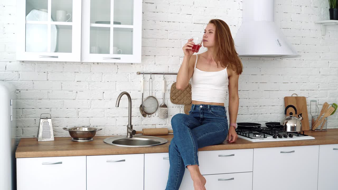 Giovane donna beve succo da un bicchiere in cucina. Cibo sano, dieta