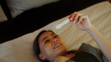woman lying in bed holding pregnancy test