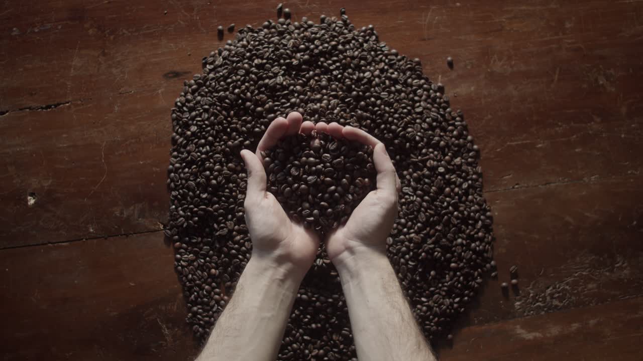 Primo piano di un filmato di mani che raccolgono chicchi di caffè tostati, che evidenzia l'interazione tattile, la ricca consistenza e i toni marrone scuro. Il tocco umano enfatizza l'artigianalità, la qualità artigianale e il