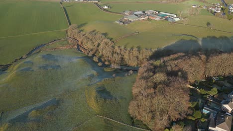 Aerial-video-of-a-peaceful-countryside-featuring-hills,-a-forest-with-fog,-and-rural-areas-on-golden-hour