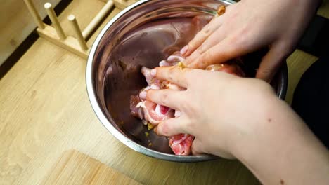 closeup shot of woman hands mixing raw chicken pieces with spices in metal bowl over on wooden countertop in the kitchen