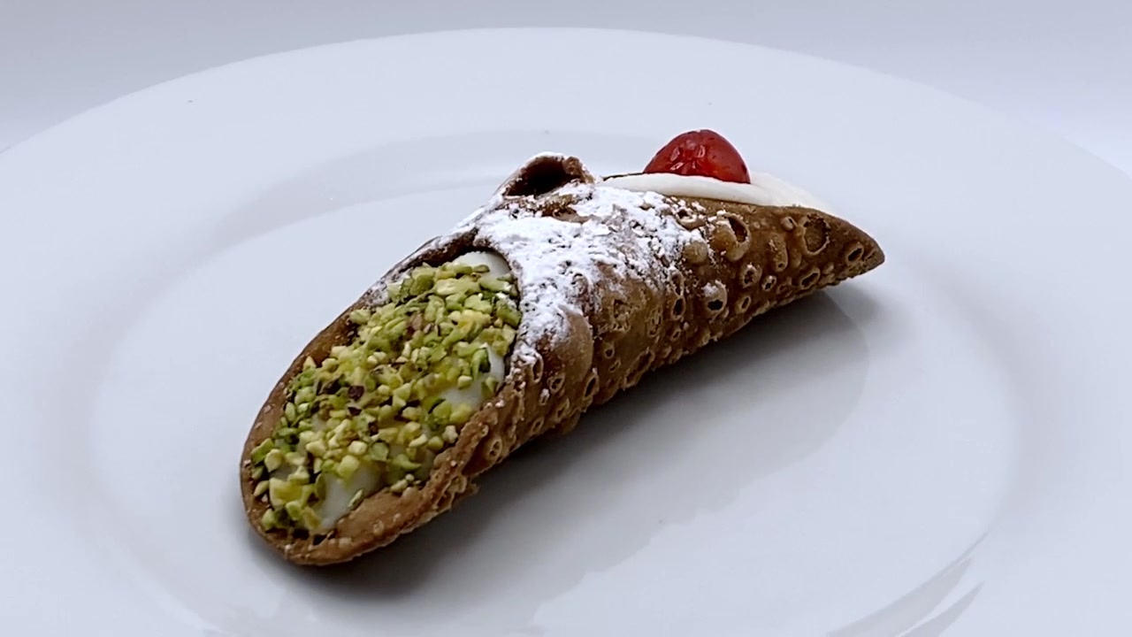 Cannolo siciliano ripieno di ricotta dolce e guarnito con ciliegia e pistacchi, isolato su sfondo bianco. Scatto in studio 4K.