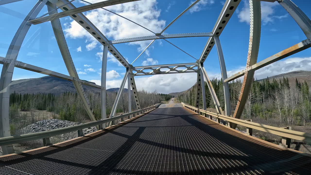POV - driving over Racing River Bridge on the Alaska Highway in Northern Rocky Mountains in British Columbia; concepts of road less traveled and adventure travels