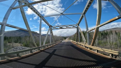 pov - driving over racing river bridge on the alaska highway in northern rocky mountains in british columbia; concepts of road less traveled and adventure travels