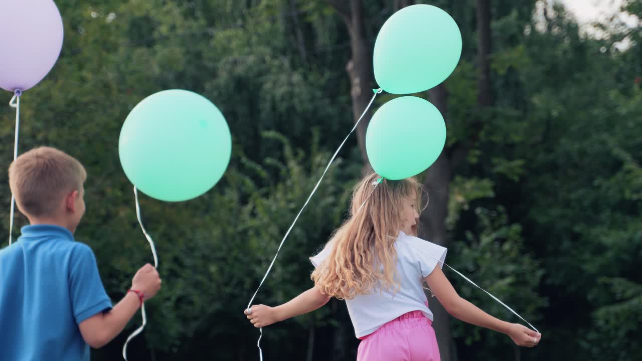 Girl and a boy in the park hold helium balloons in their hands. Holiday games for children