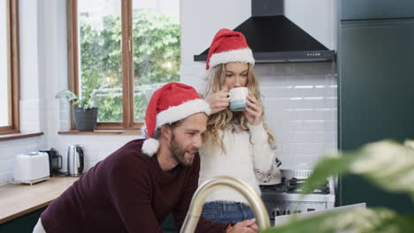 Vielfältiges-Paar-Mit-Weihnachtsmützen,-Das-Einen-Laptop-Für-Einen-Weihnachtsvideoanruf-In-Zeitlupe-Verwendet