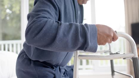 Mid-section-of-biracial-senior-man-using-walking-frame-at-home,-slow-motion