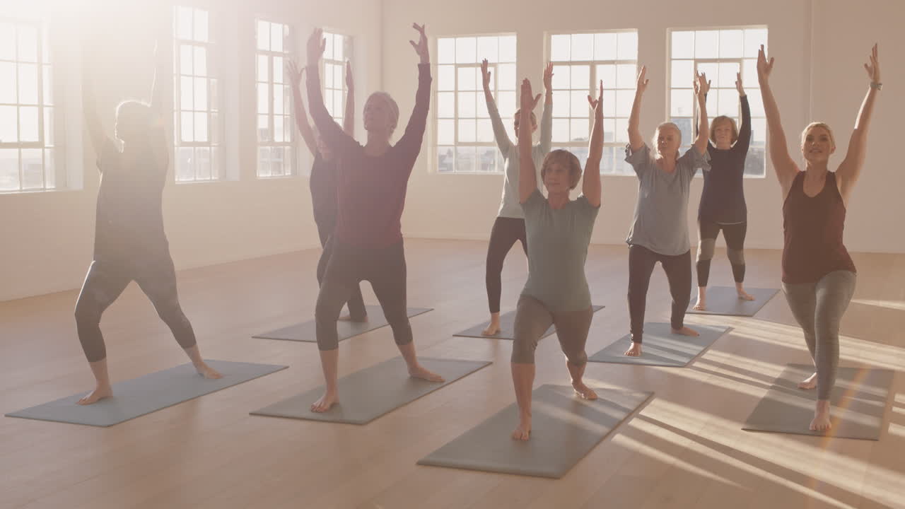 전사 포즈를 연습하는 건강한 성숙한 여성들의 요가 수업은 일출 스튜디오에서 아침 체력 운동을 즐기고 있습니다.