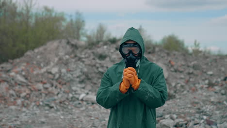 virologist man in protective costume and respirator gas mask standing in a deserted city at the industrial factory and a lot of trash background